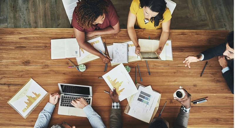 overhead shot of people meeting at a large table reviewing notes and laptop