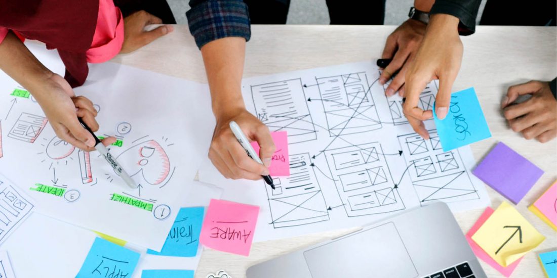 close up of multiple hands drawing work sketches on desk