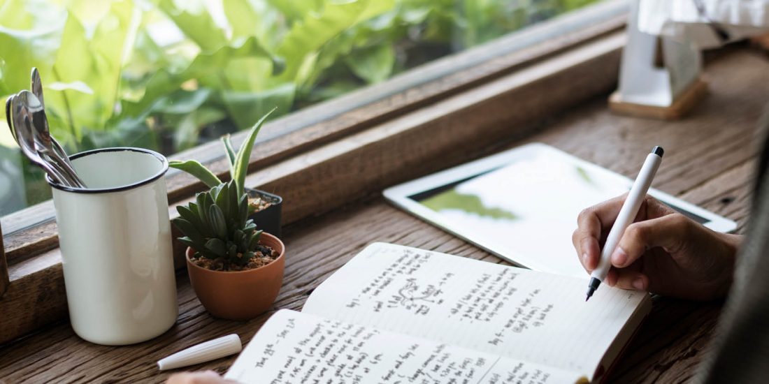 close up pf notebook on desk and hand with pen writing in book