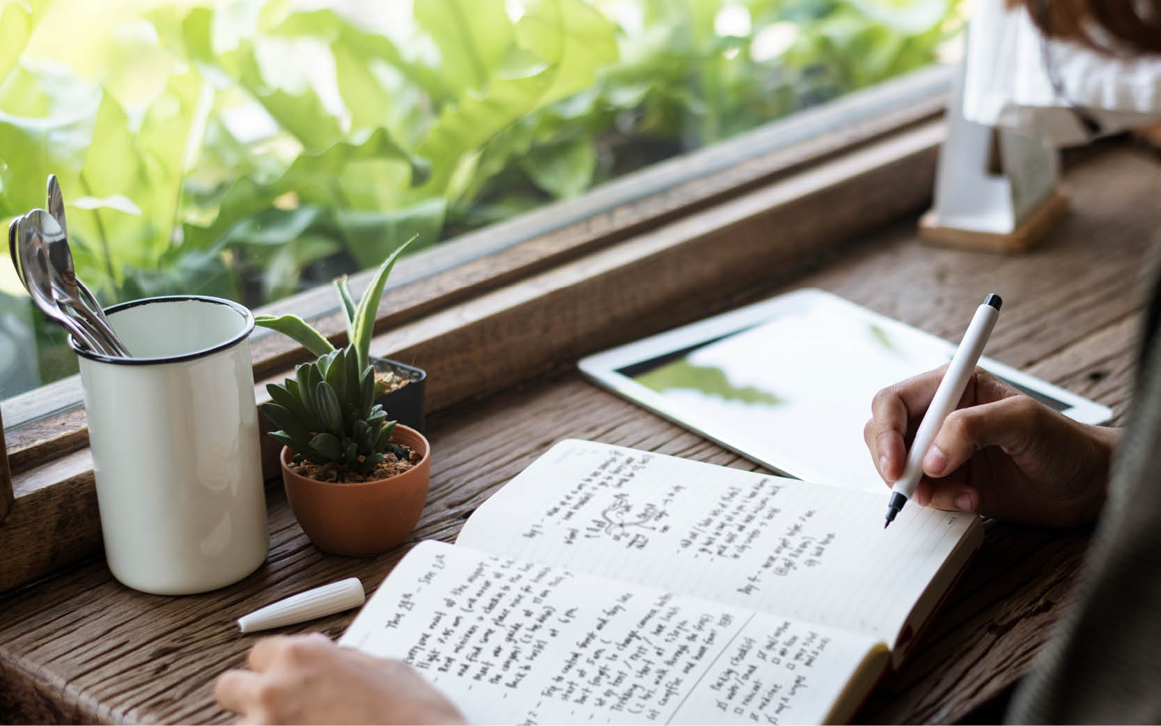 close up pf notebook on desk and hand with pen writing in book